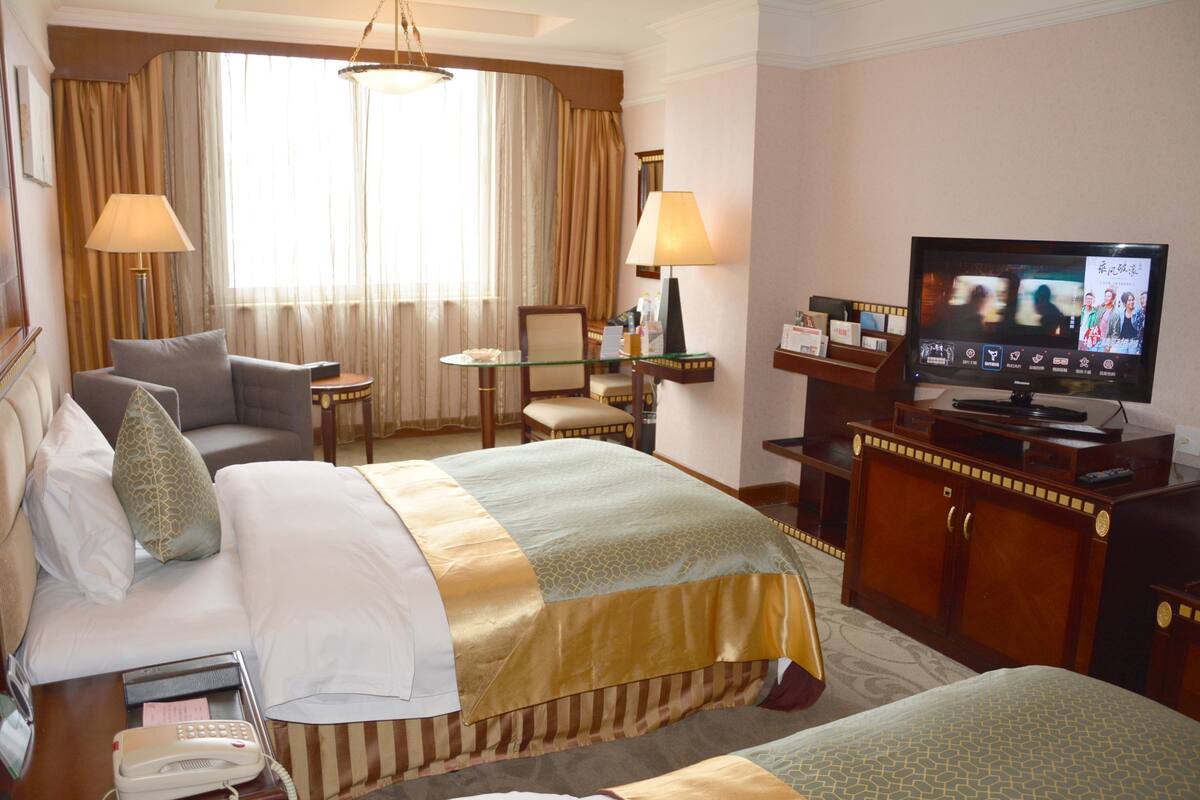 Une chambre d’hôtel avec un grand lit, un lit plus petit, une télévision, un bureau avec une lampe, une chaise et une lampe de bureau.