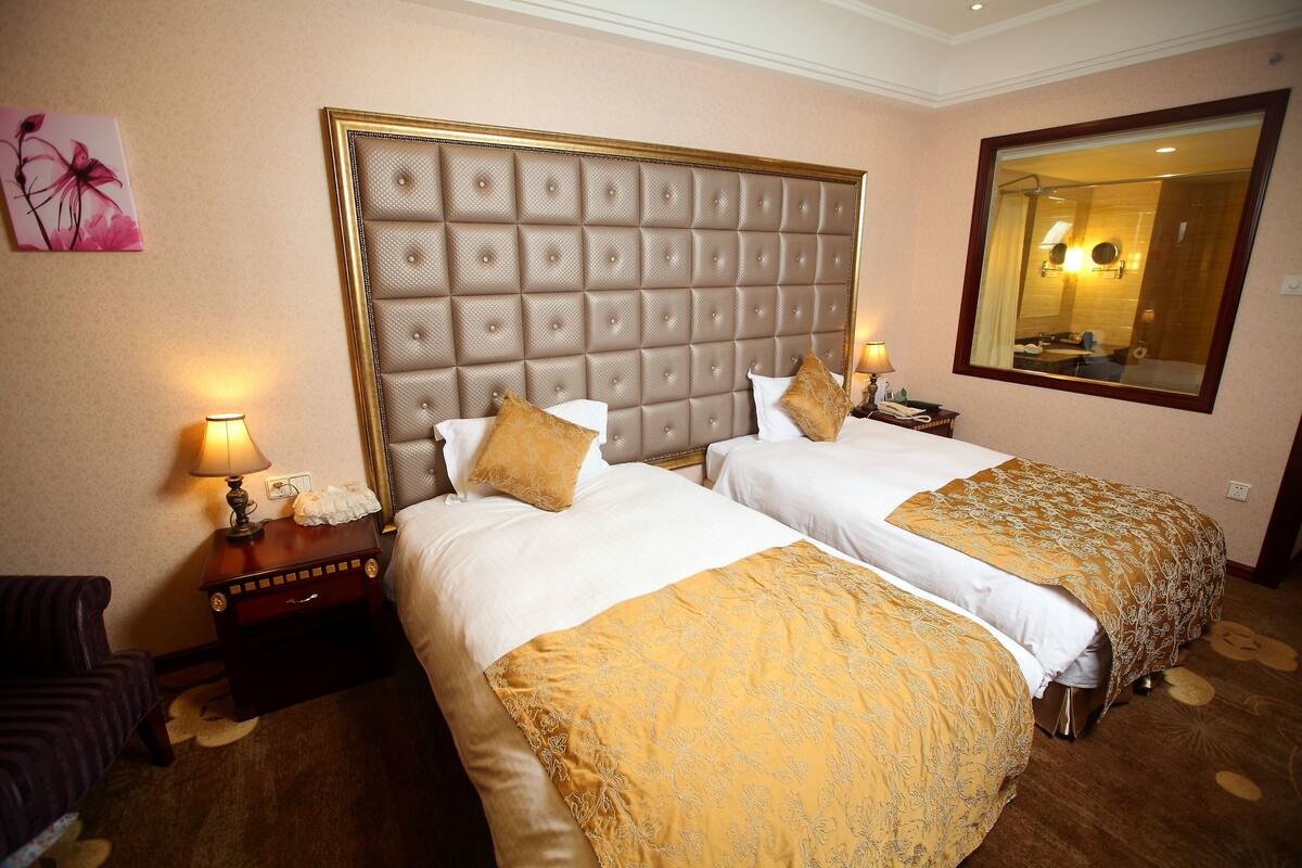 Une chambre d’hôtel avec deux lits, un grand miroir et une table de chevet avec une lampe.