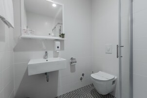 A bathroom with a white sink, mirror, toilet, and shower.