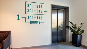 Habitación de hotel con un cartel en la pared que indica los números de habitación de 301 a 315, 201 a 215 y 101 a 115.