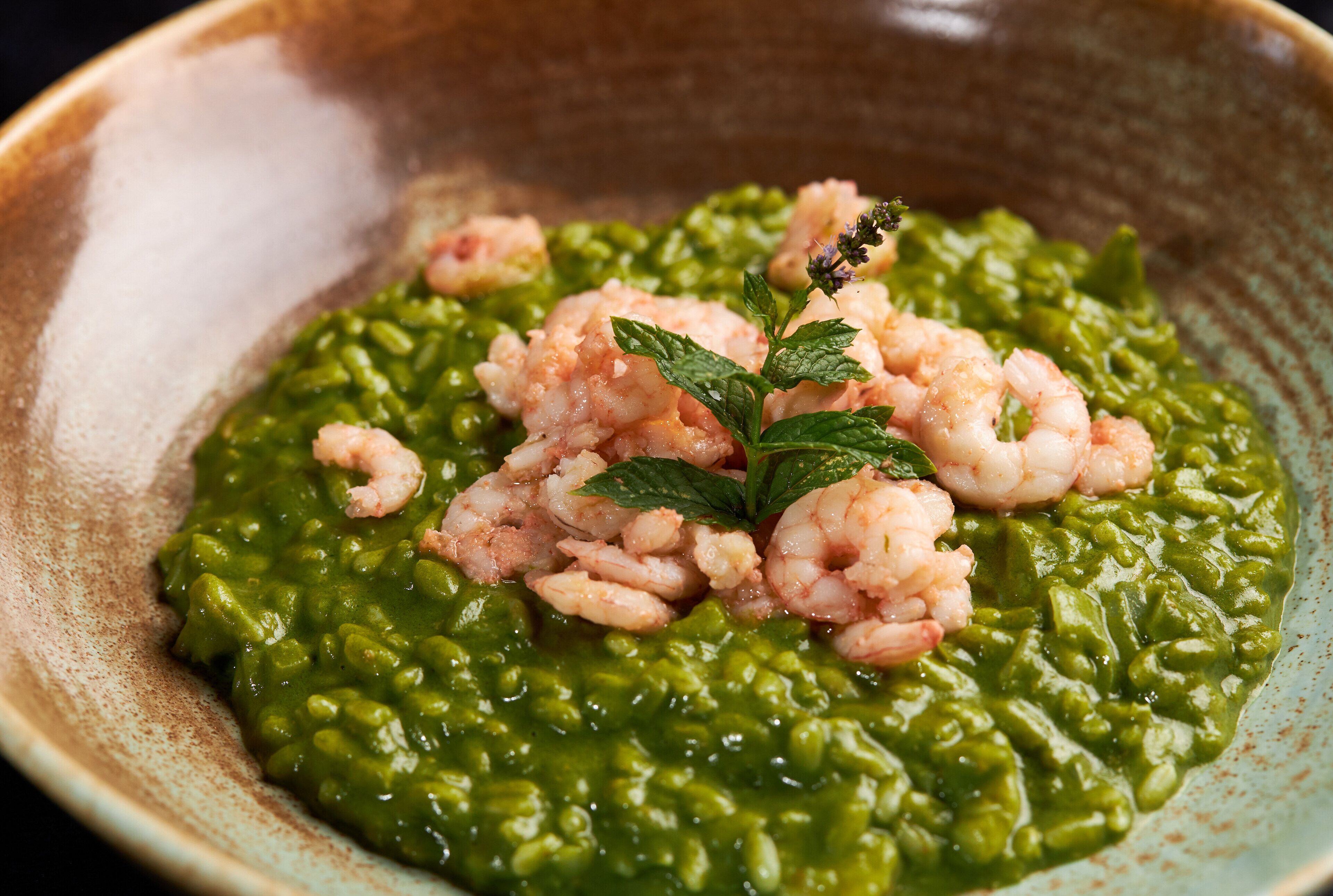 A bowl of green risotto with shrimp and a mint garnish.