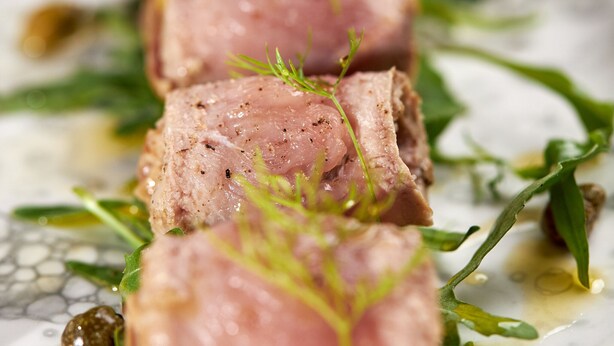Une vue rapprochée d’un plat composé de viande en tranches, de légumes verts et d’une sauce.