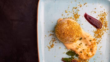 Un dessert servi dans une assiette bleu clair, parsemé de miettes et décoré de feuilles de menthe.