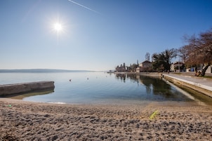 Un lago tranquilo con cielo despejado, una playa de arena y una hilera de edificios a lo largo de la orilla.