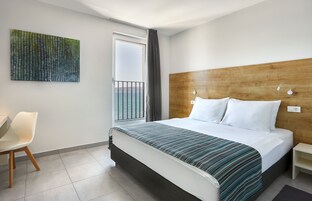 Una habitación de hotel moderna con una cama grande, un cabecero de madera, vista al mar desde un balcón y una obra de arte contemporánea en la pared.