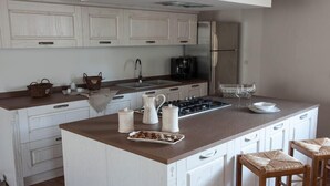 Een keuken met witte kasten, een centraal eiland met een bruin aanrecht, een gasfornuis en een koelkast.