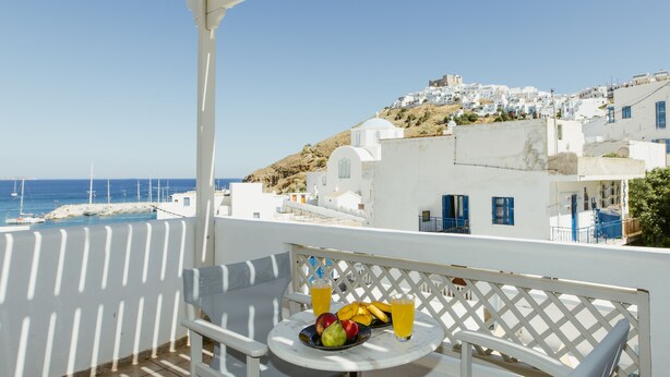 A balcony with a table set for two, overlooking a coastal town with white buildings and the sea. - Viva Mare Studios (Astypalaia)