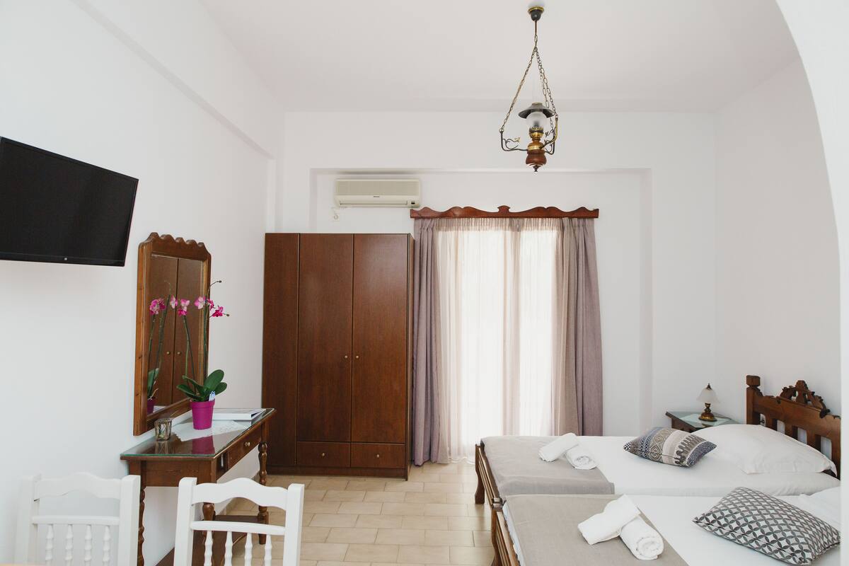 A bedroom with a bed, a wooden wardrobe, a desk with a mirror, and a television on the wall.