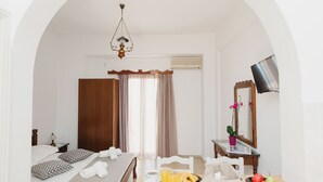 A hotel room with a bed, a dining table with breakfast, a TV, and a window with curtains. - Viva Mare Studios (Astypalaia)