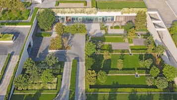 Vue aérienne d’un complexe immobilier moderne composé de plusieurs bâtiments, dont un grand bâtiment central doté de grandes fenêtres en verre, le tout entouré de jardins et d’allées bien entretenus.