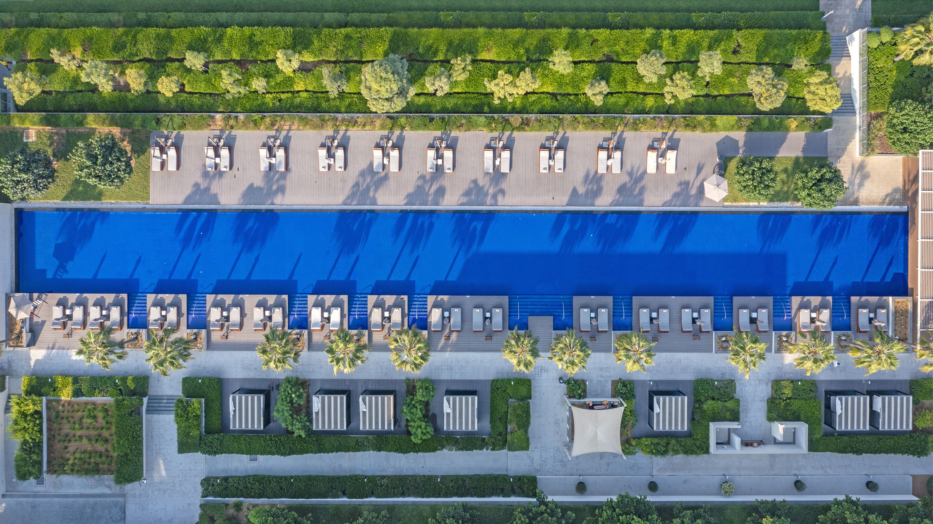 An aerial view of a hotel with a large swimming pool, sun loungers, and a well-maintained garden.