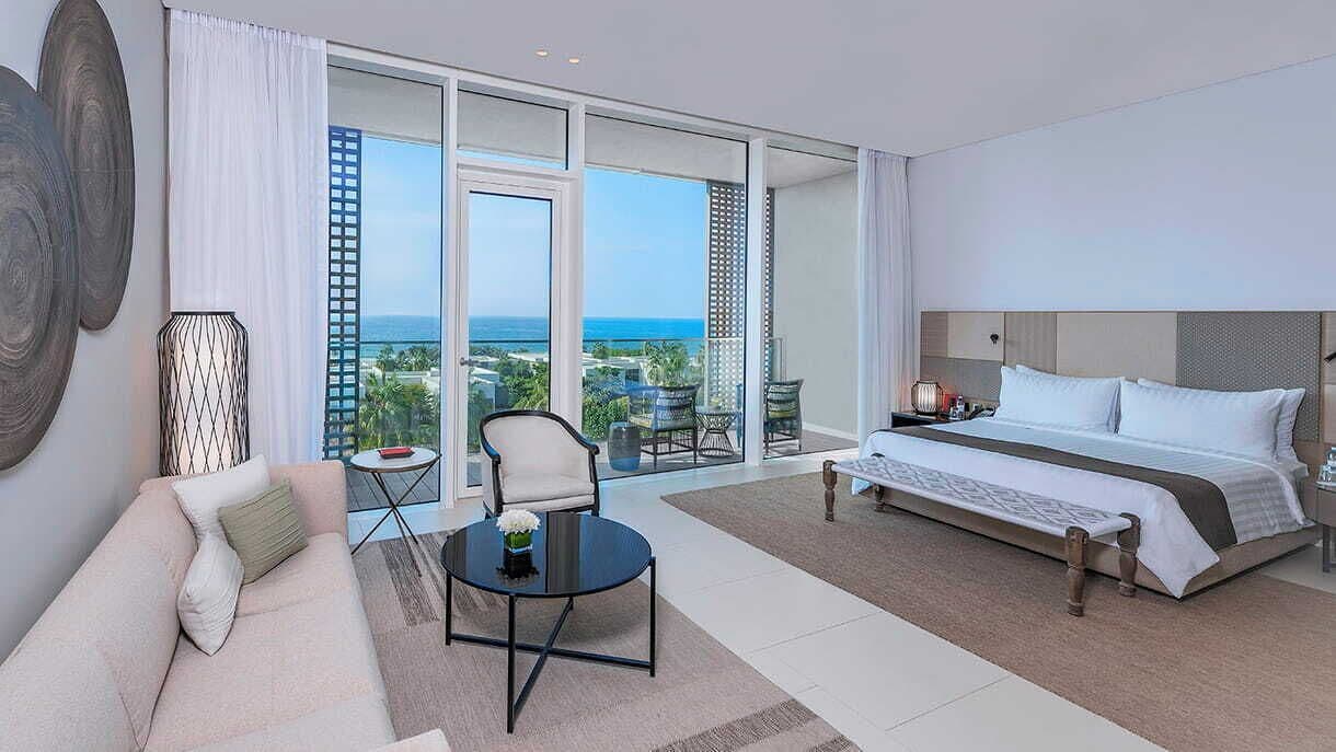 Een hotelkamer met een bed, een slaapbank, een bijzettafeltje en uitzicht op de oceaan.