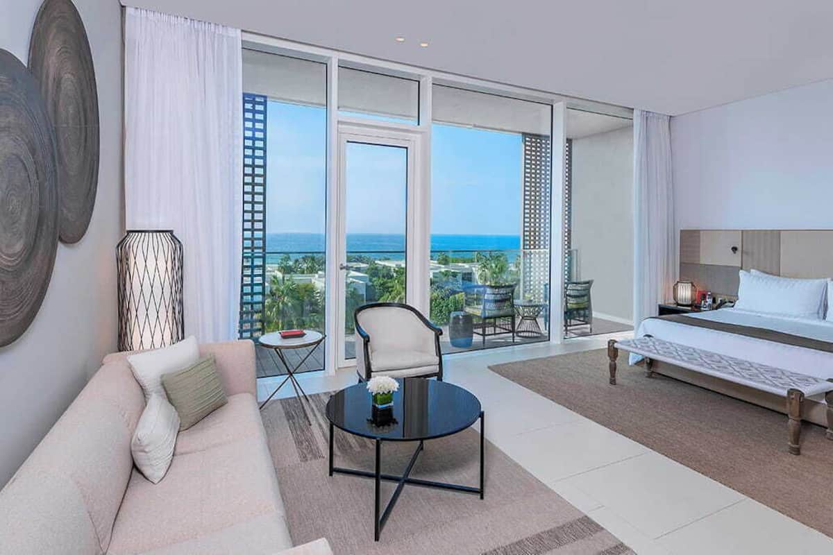 A hotel room with a bed, a sofa, a coffee table, and a view of the ocean.