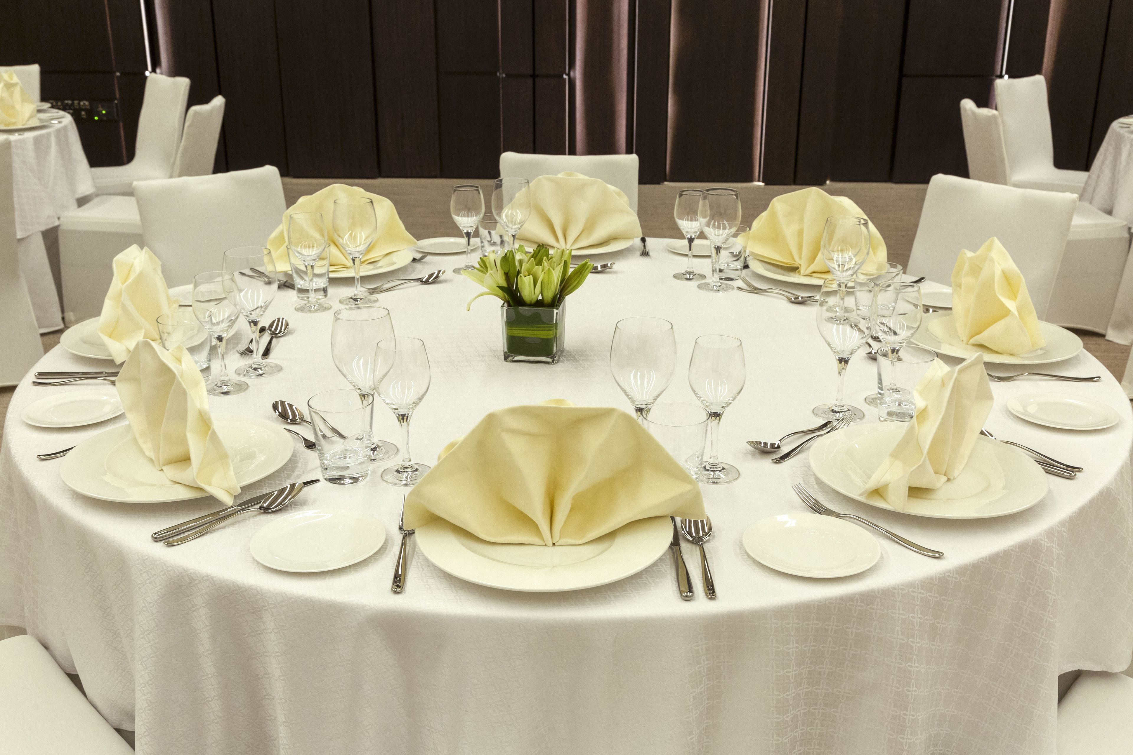A round dining table set with white tablecloths, neatly arranged plates, cutlery, and glassware.