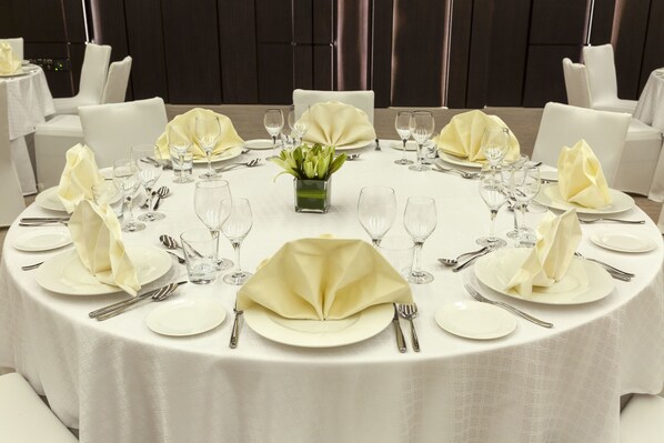 A round dining table set with white tablecloths, neatly arranged plates, cutlery, and glassware.