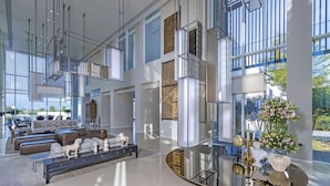 Ett rymligt och modernt vardagsrum med högt tak, stora fönster och ett centralt placerat glasbord som reflekterar inredningen.