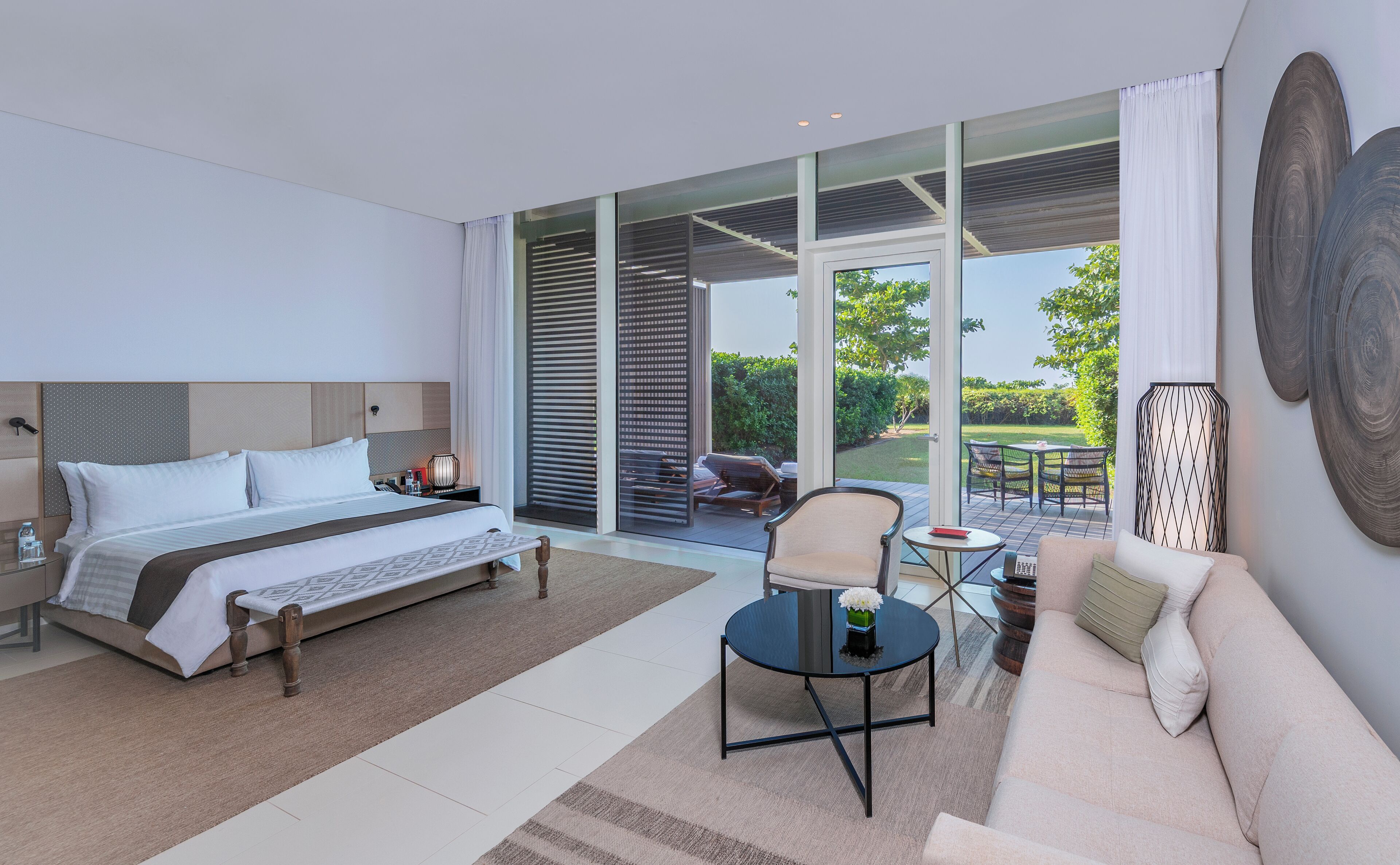 Een moderne hotelkamer met een groot bed, een bank, een kleine tafel en uitzicht op de tuin door de glazen deur.