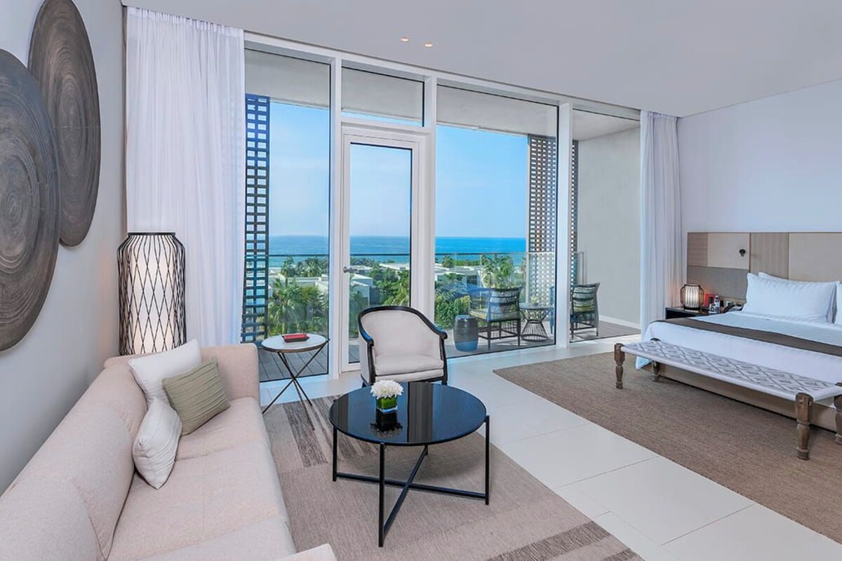 A hotel room with a bed, a sofa, a coffee table, and a view of the ocean.