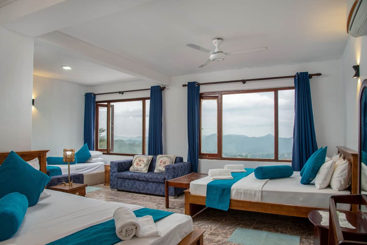A hotel room with two beds, a sofa, a ceiling fan, and large windows with curtains.