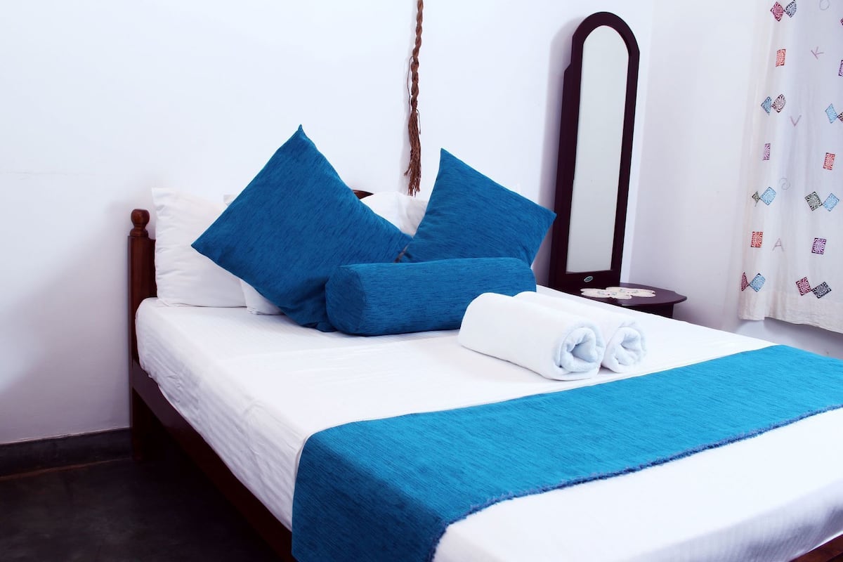 A neatly made bed with blue bedding, a white pillow, and a rolled towel.