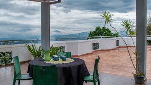 Un patio exterior con mesa y sillas, vista al mar y plantas en macetas.
