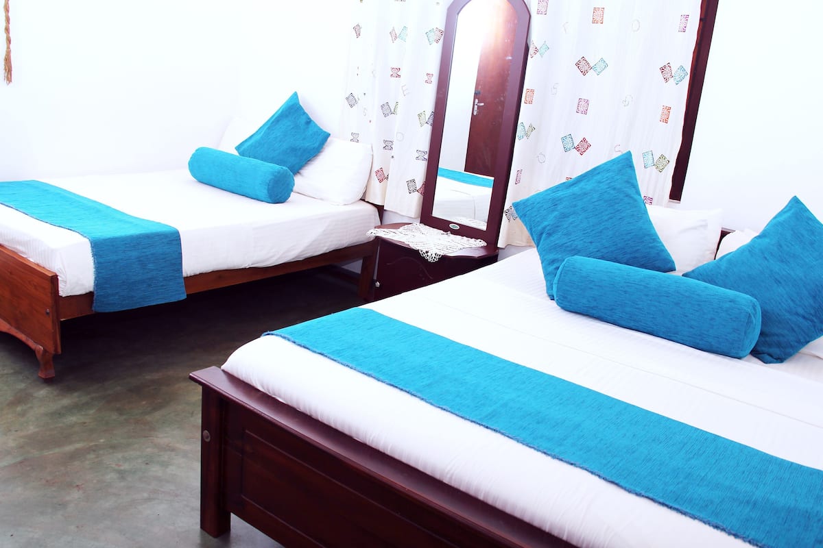 Two single beds with blue pillows and a wooden headboard, a nightstand with a mirror, and a patterned curtain.