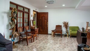 Una habitación con puerta de madera, un sillón verde, una mesa de comedor con sillas y un televisor.