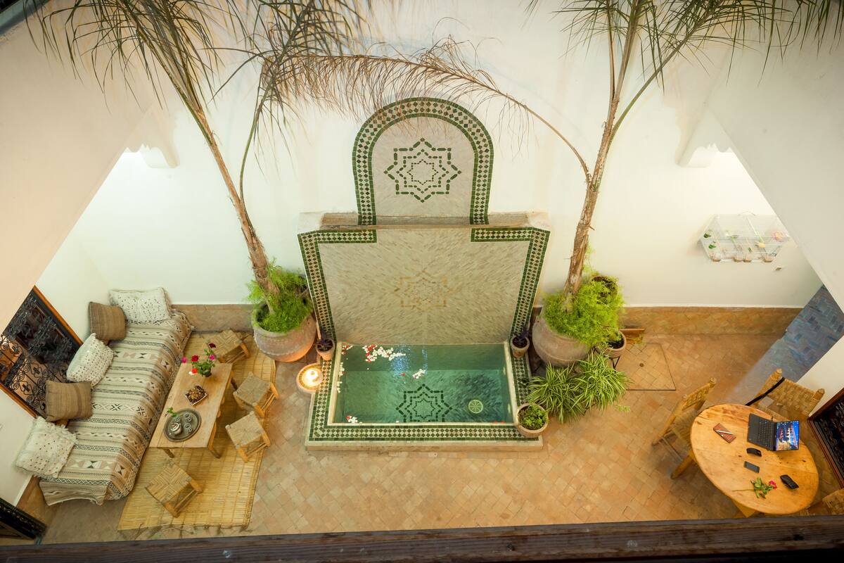 A high-ceilinged room with a central seating area featuring a patterned sofa, a small table with decorative items, and a water feature.