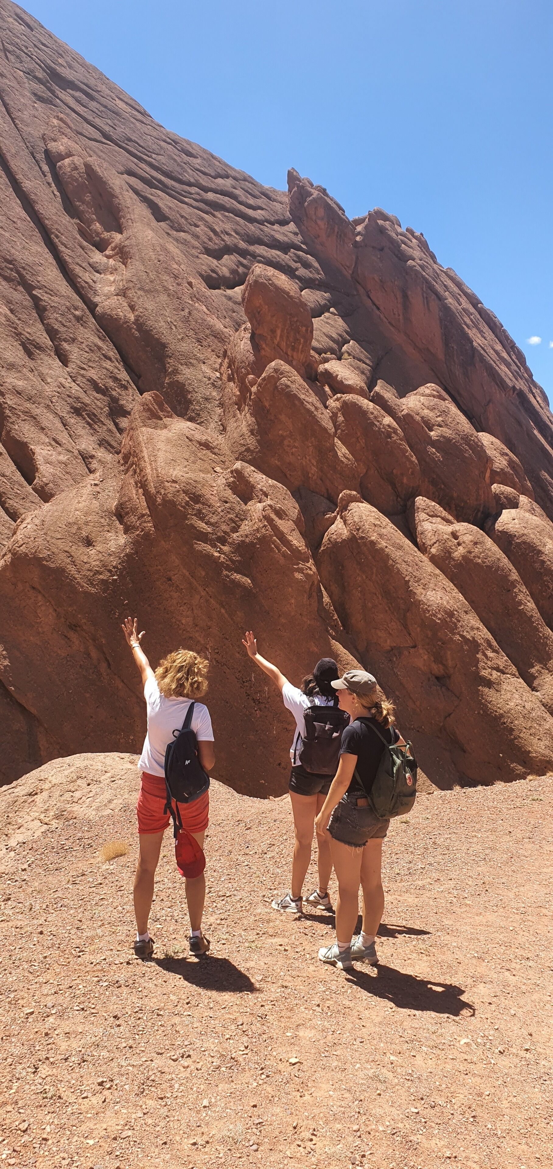 Three people standing on a rocky terrain with a large rock formation in the background.