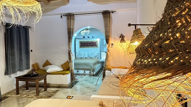 Une pièce avec un lit, une petite table, un luminaire suspendu et une vue sur une autre pièce.