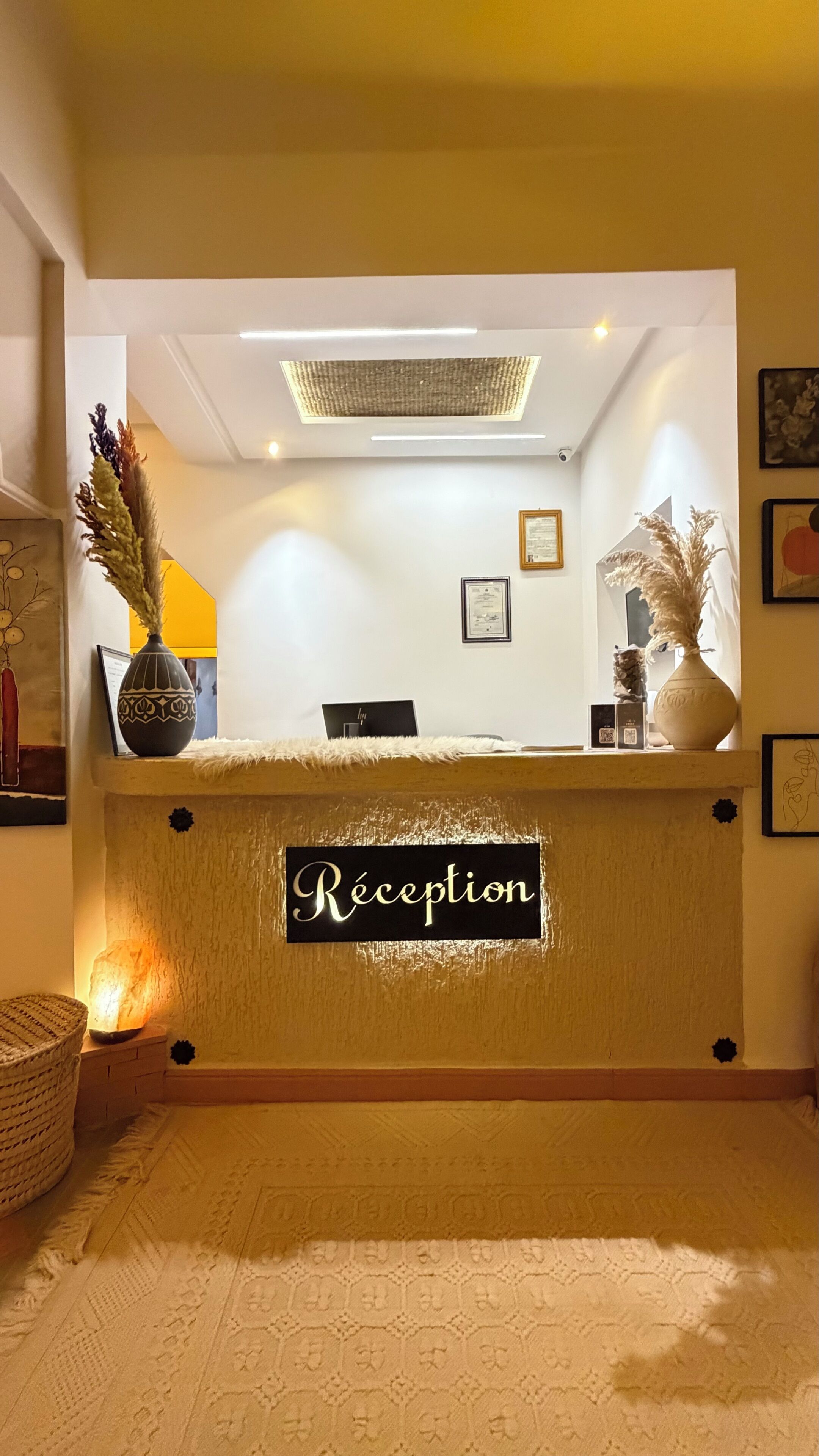 A reception desk with a sign reading 'Réception,' a laptop on the counter, and decorative vases.