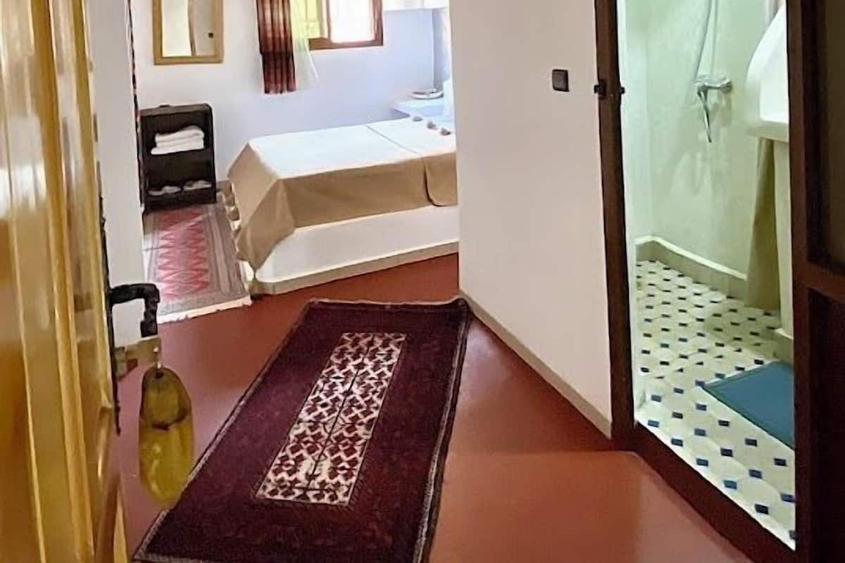 Une pièce avec un plafond en bois, un lit, une petite table, un miroir et une fenêtre avec des rideaux.