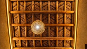 Une pièce avec une structure de plafond en bois, un luminaire suspendu, un tableau encadré, une table avec des assiettes et une chaise.