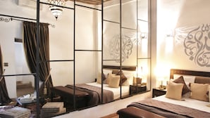 Une chambre d’hôtel avec un séparateur en miroir, un lit avec de nombreux oreillers, une table de chevet avec une lampe et un élément décoratif mural.