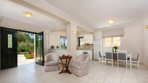 A spacious living area with a dining table and chairs, a small round table, and a kitchen in the background. - Il Tesori Dassia Villas (Corfu)