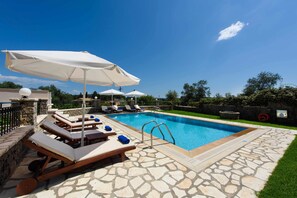 A swimming pool with lounge chairs and umbrellas, surrounded by stone tiles and greenery. - Il Tesori Dassia Villas (Corfu)