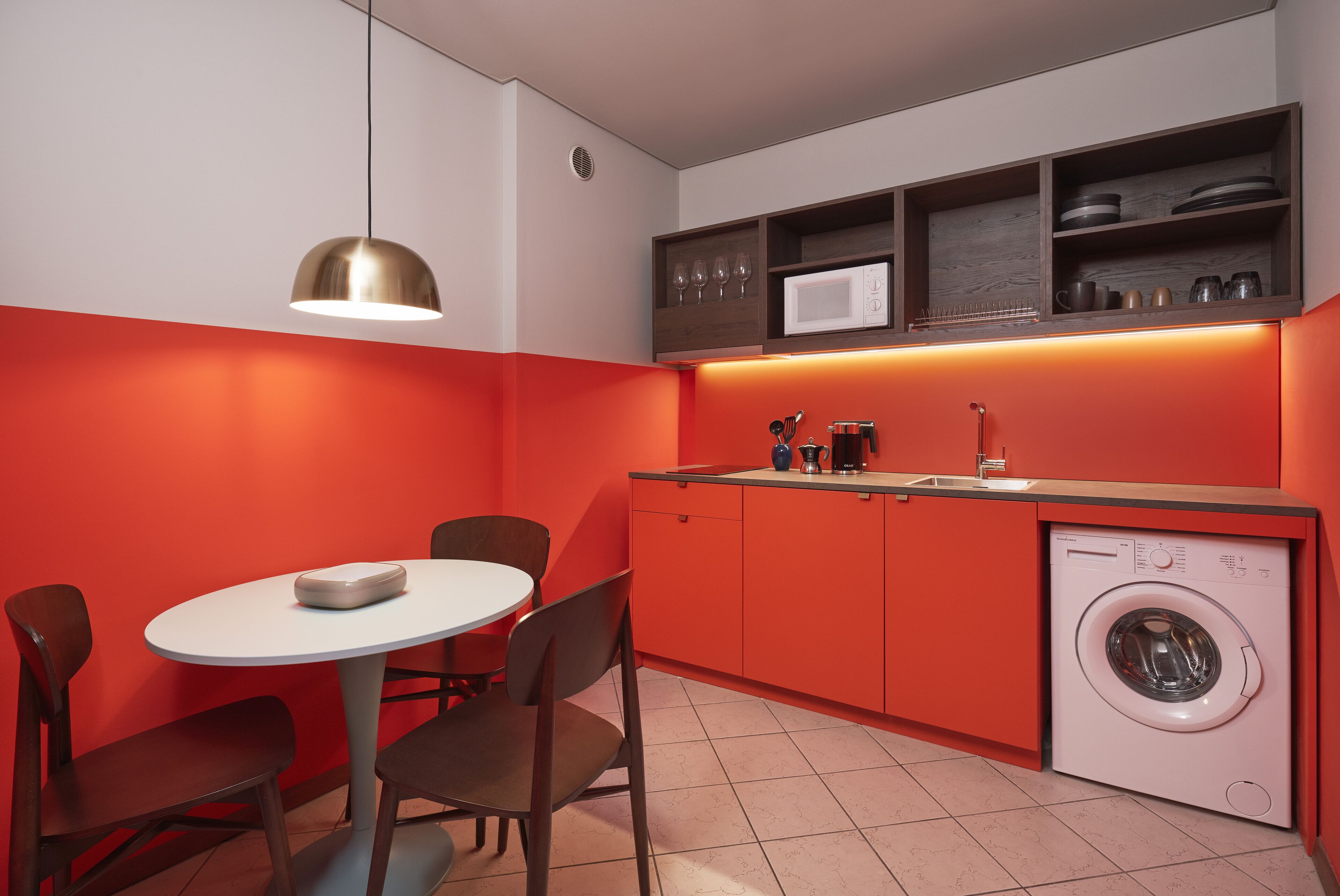 A compact kitchen with a dining area, a washing machine, and a pendant light.
