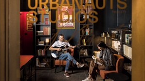 A cozy room with a guitar player and a woman seated, surrounded by bookshelves and a red wall. - Urbanauts Studios Minelli (Trieste)