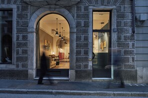 A building with a stone facade, an arched entrance, and a visible interior with furniture and lighting. - Urbanauts Studios Minelli (Trieste)