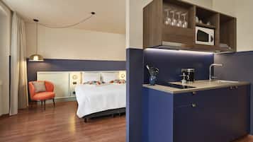 Una camera d'albergo moderna con un letto, una poltrona arancione, una kitchenette con forno a microonde e macchina del caffè.