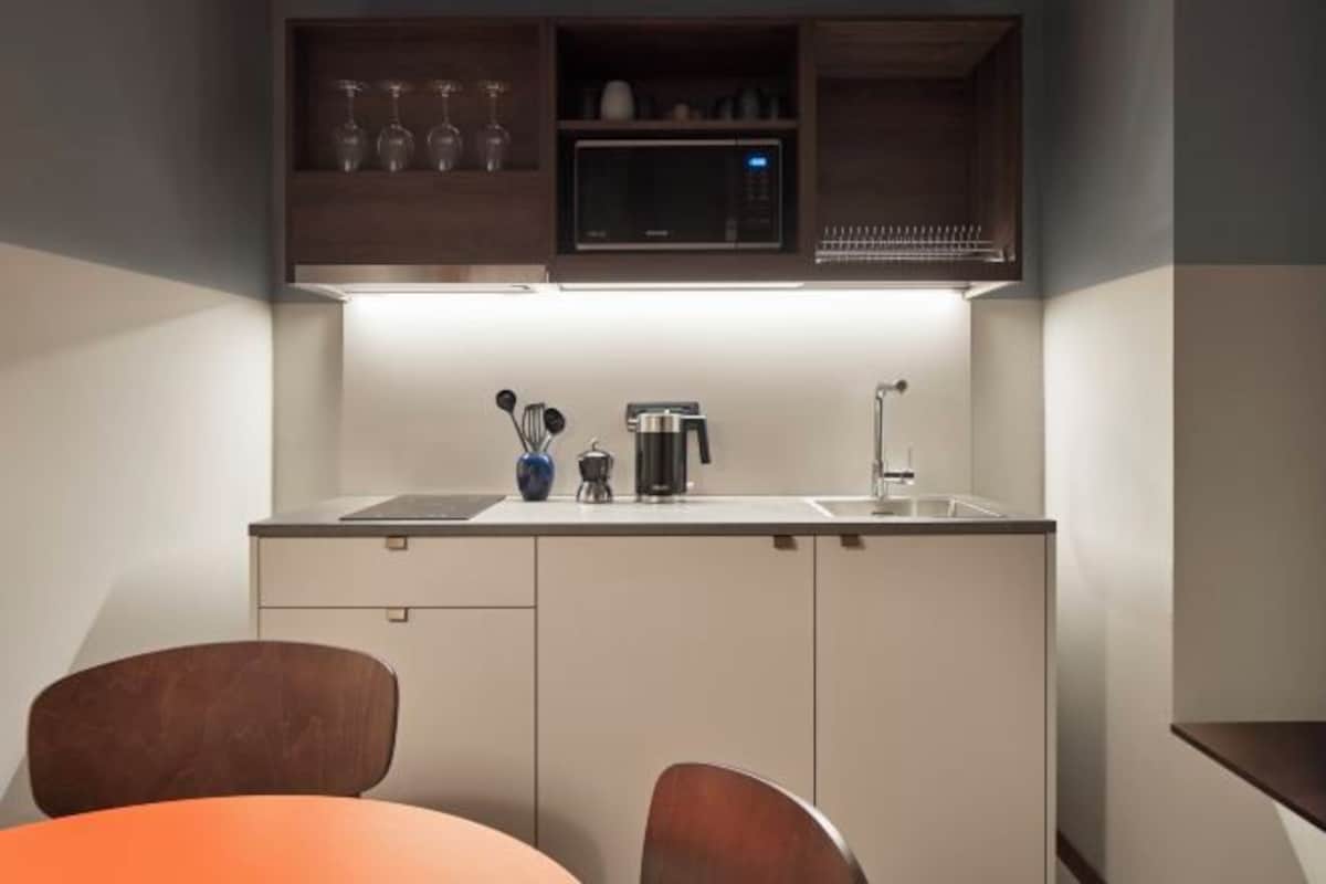A compact kitchen with a microwave, toaster, and sink. There are two chairs and a table in the foreground.