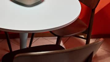 Una mesa redonda con superficie blanca y un objeto cuadrado encima. Una silla marrón con asiento acolchado está colocada frente a la mesa.