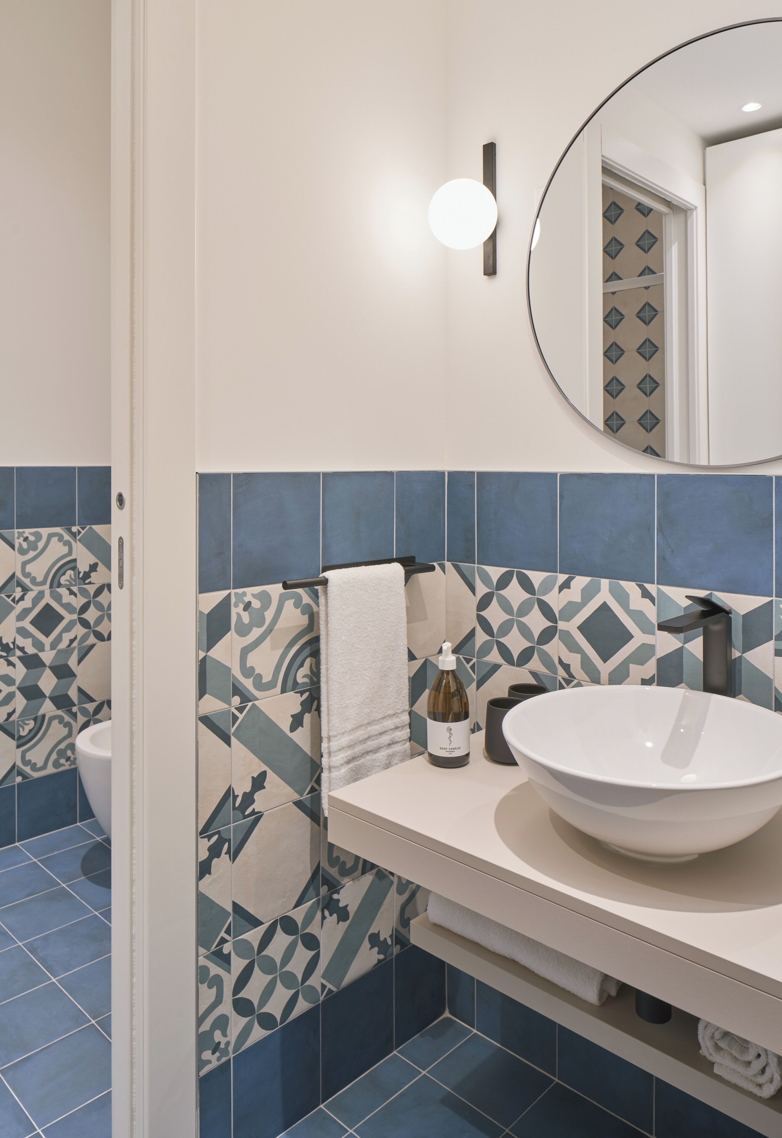 A bathroom with a white sink, a round mirror, and patterned tiles.