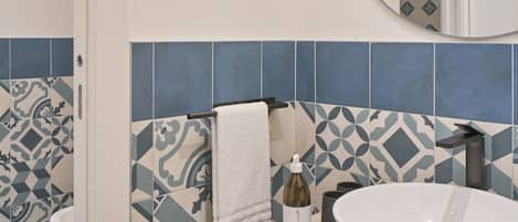 A bathroom with a white sink, a round mirror, and patterned tiles.
