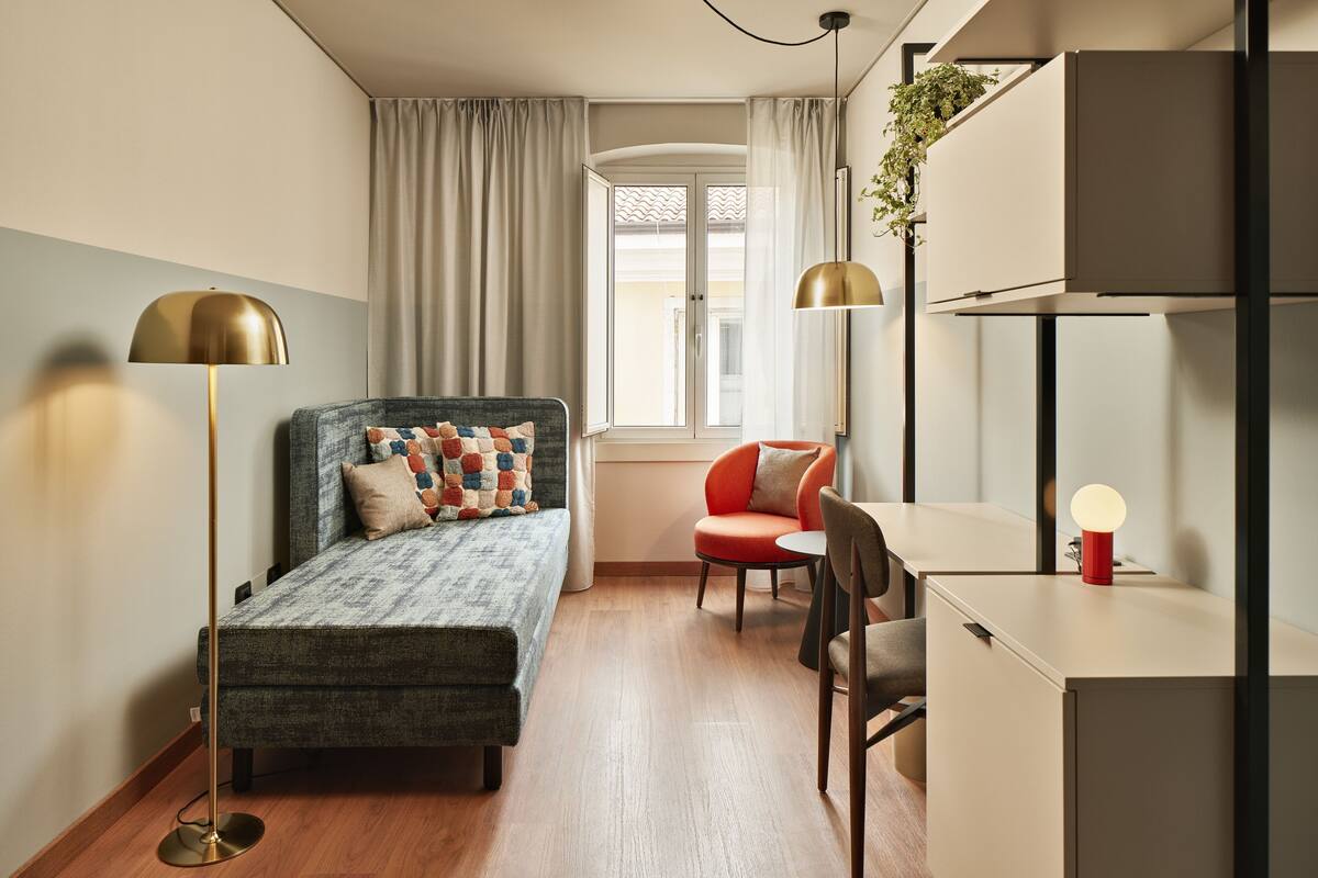 A modern bedroom with a bed, a desk, a chair, and a floor lamp.