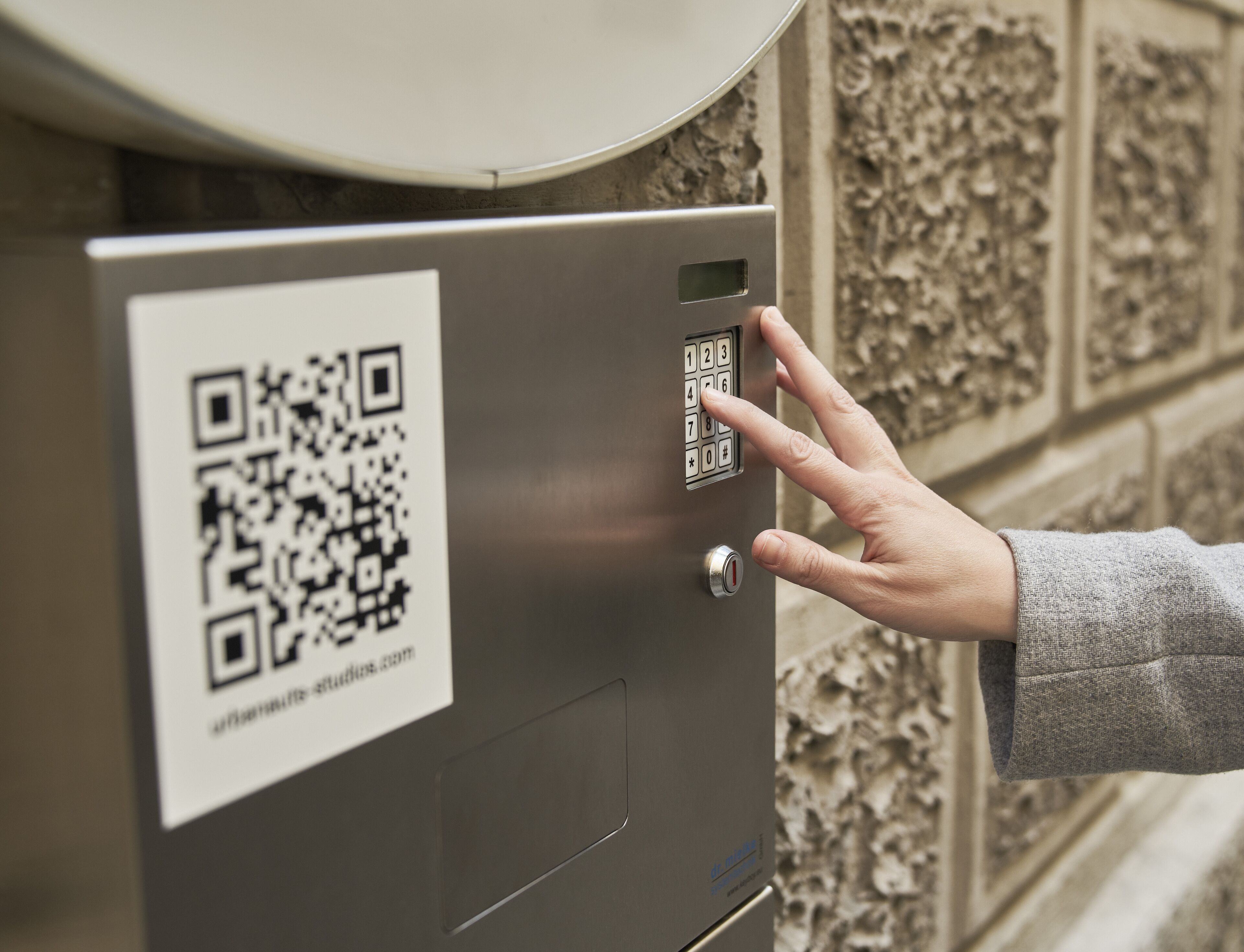 A hand interacting with a keypad on a metallic box with a QR code.