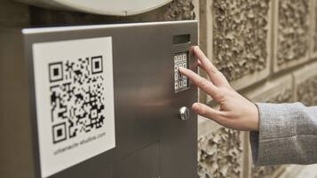 A hand interacting with a keypad on a metallic box with a QR code.