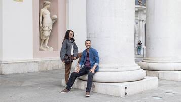 Un uomo e una donna seduti su una panchina di pietra di fronte a un edificio classico con colonne e una statua.
