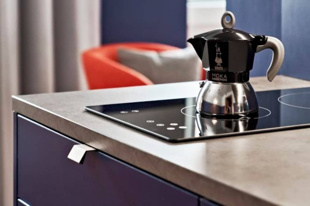 A modern kitchen with a black induction cooktop and a Moka pot on it.