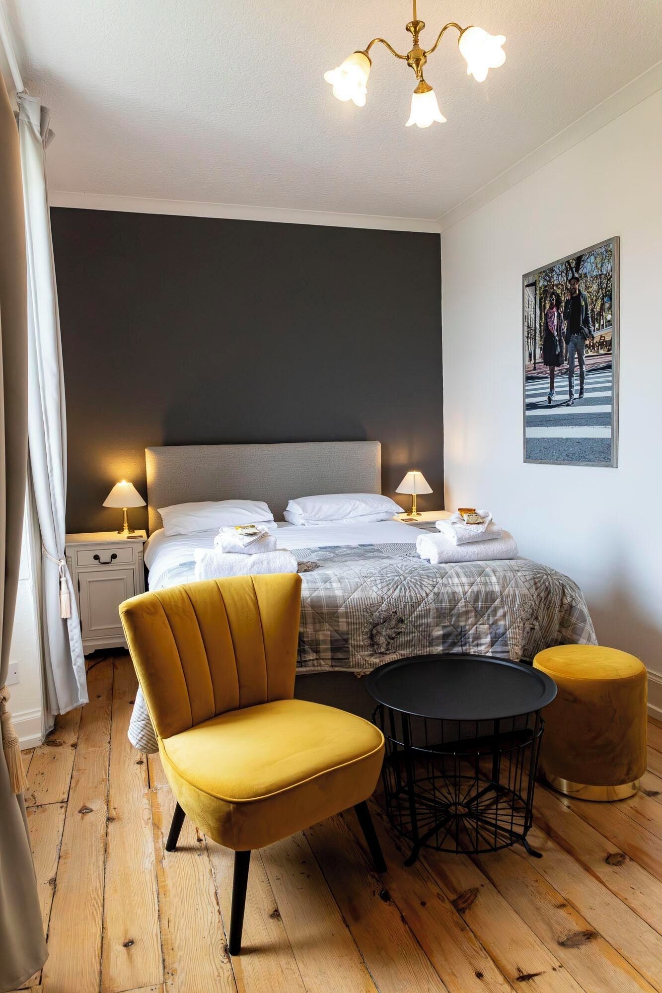 A bedroom with a bed, two bedside tables, a chair, a round table, and a hanging light fixture.